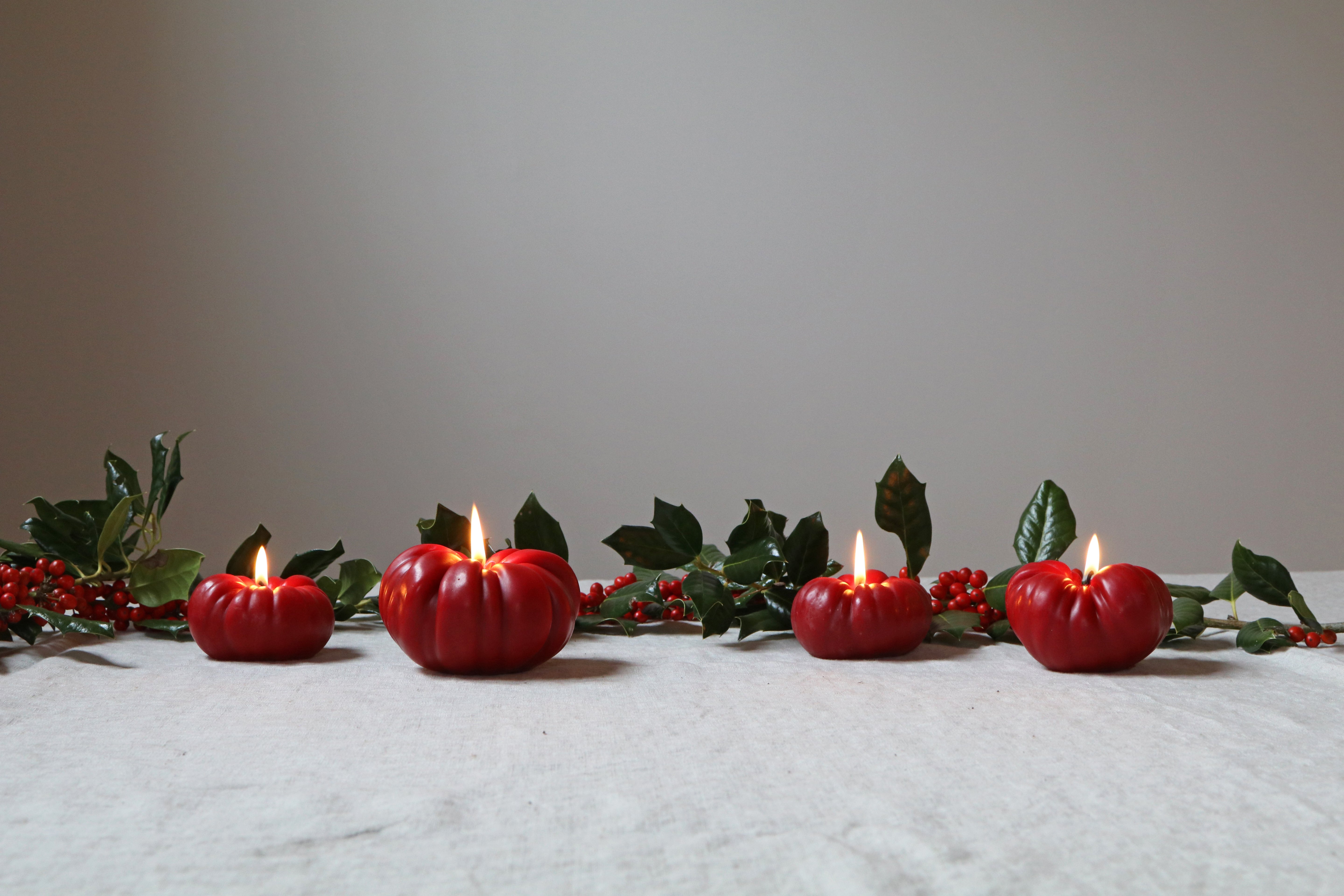Decorative red candles in pumpkin shapes with green leaves on a white surface.