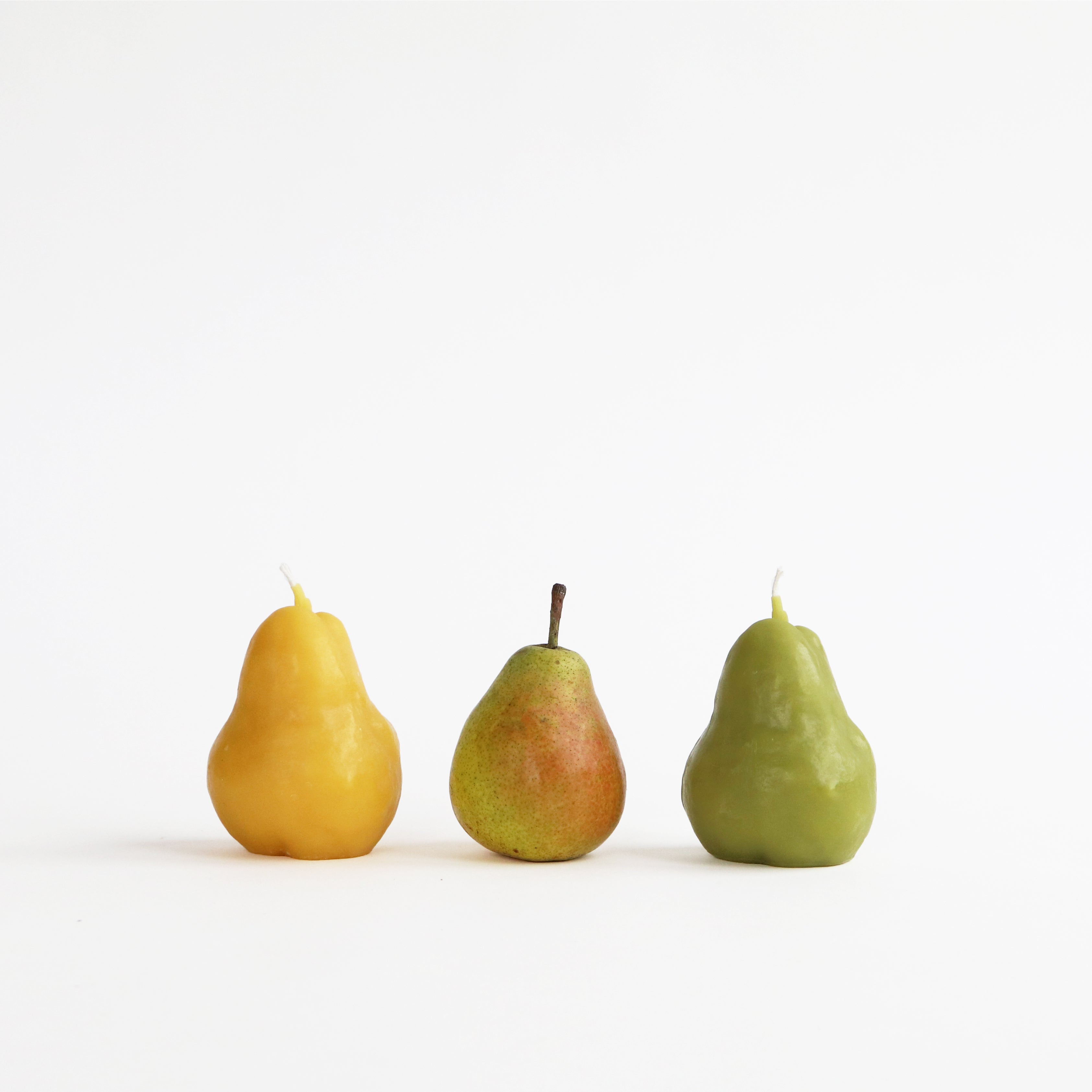 Three pears of different colors on a white background. One is a beeswax candle.