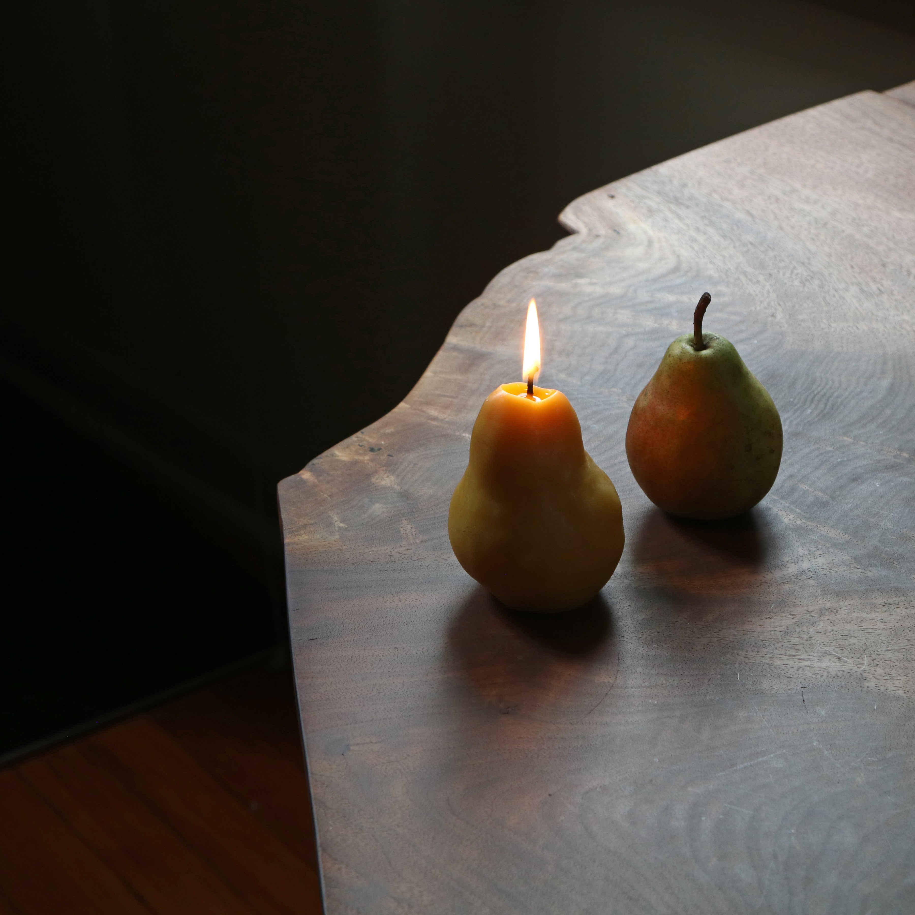 Pear-shaped candle and real pear on a wooden surface with dark background