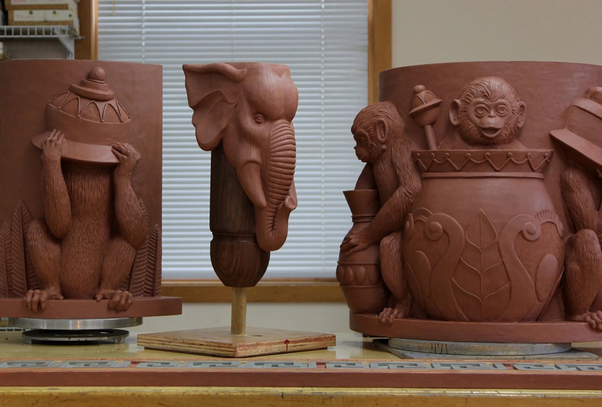 Terracotta sculptures including a monkey, elephant, and pot on a wooden surface.