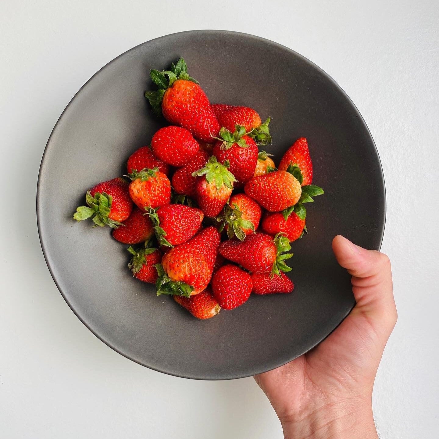 hand holding metal black bowl with strawberries inside