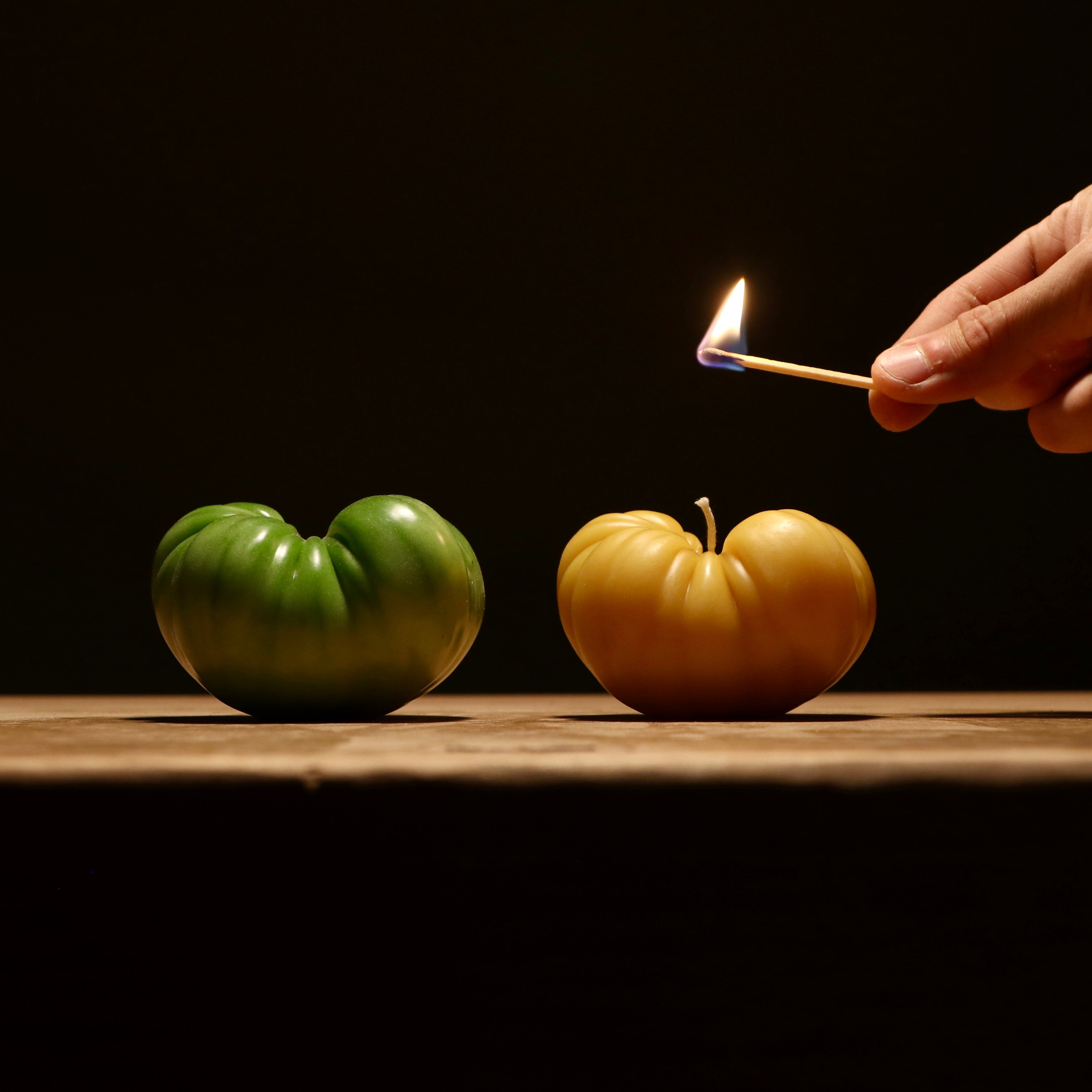 beeswax tomato candle being lit next to tomato it was molded from
