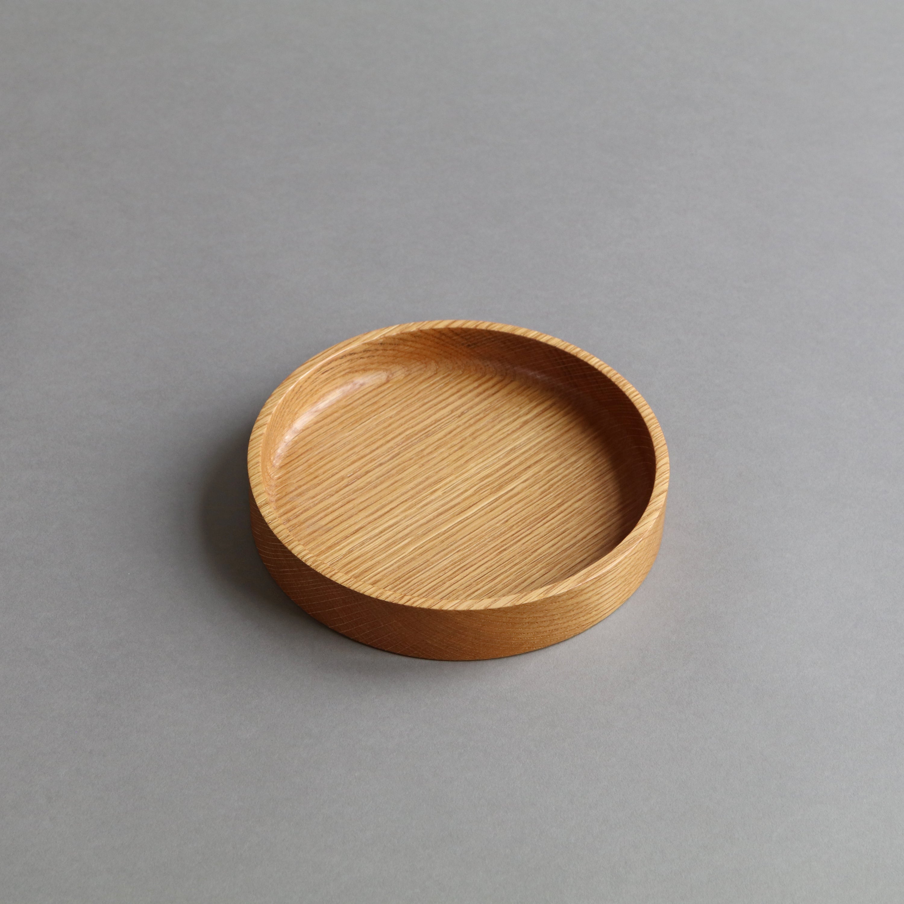 A round, shallow wooden tray with a smooth, light brown wood grain finish, photographed on a neutral gray background.