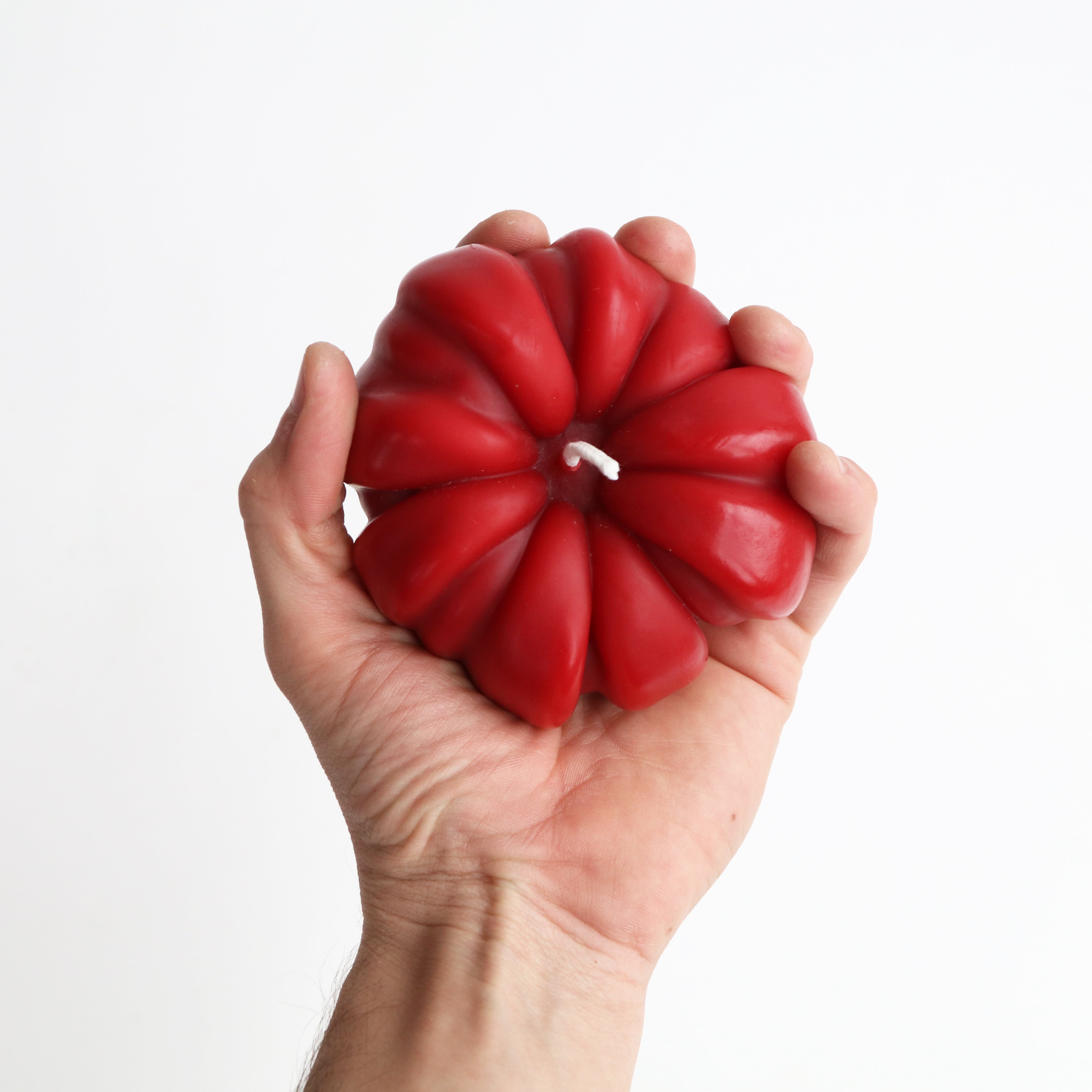 Hand holding a red, tomato shaped candle against a white background