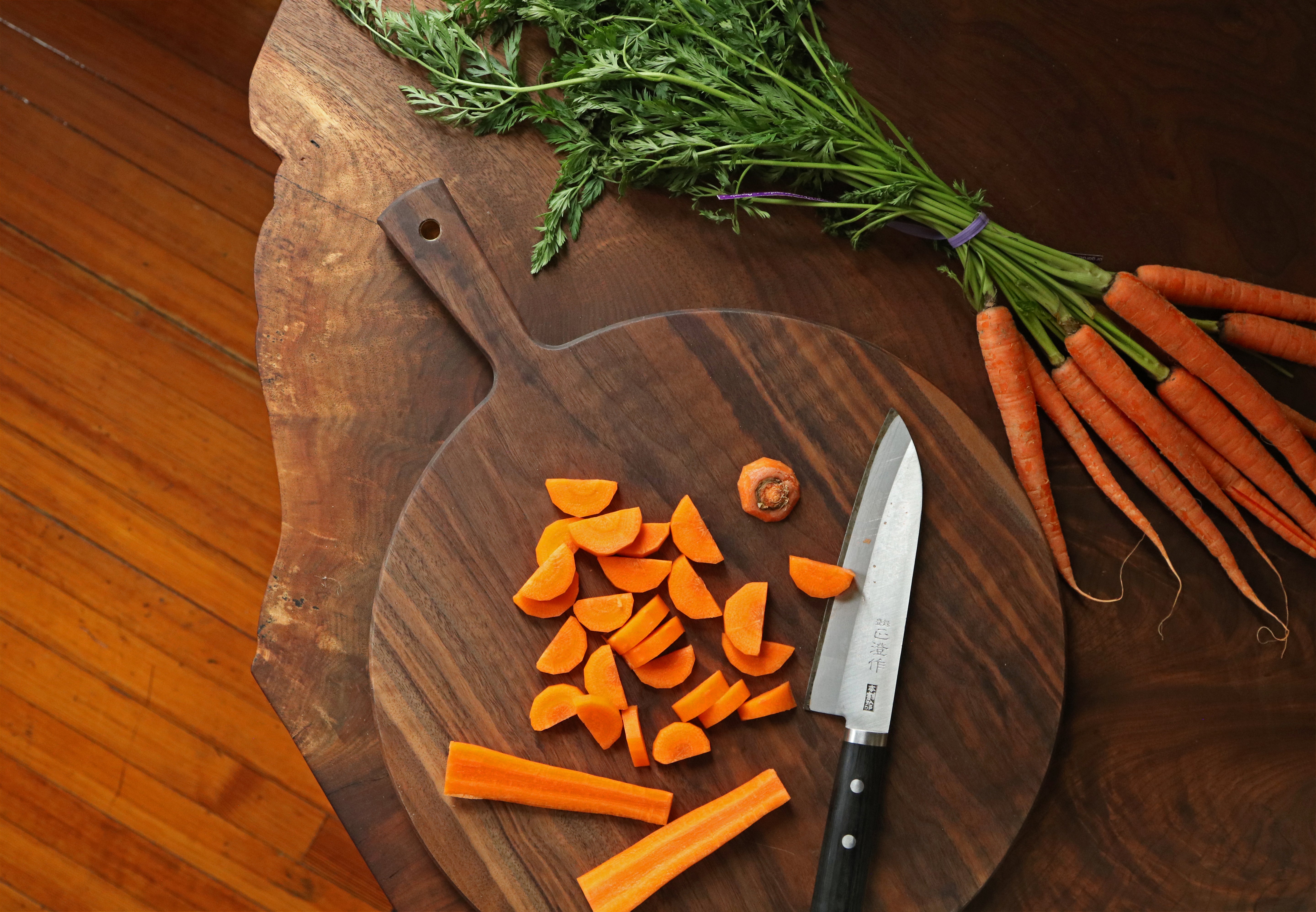 Carrots on a wooden cutting board with a knife and some whole carrots beside it.