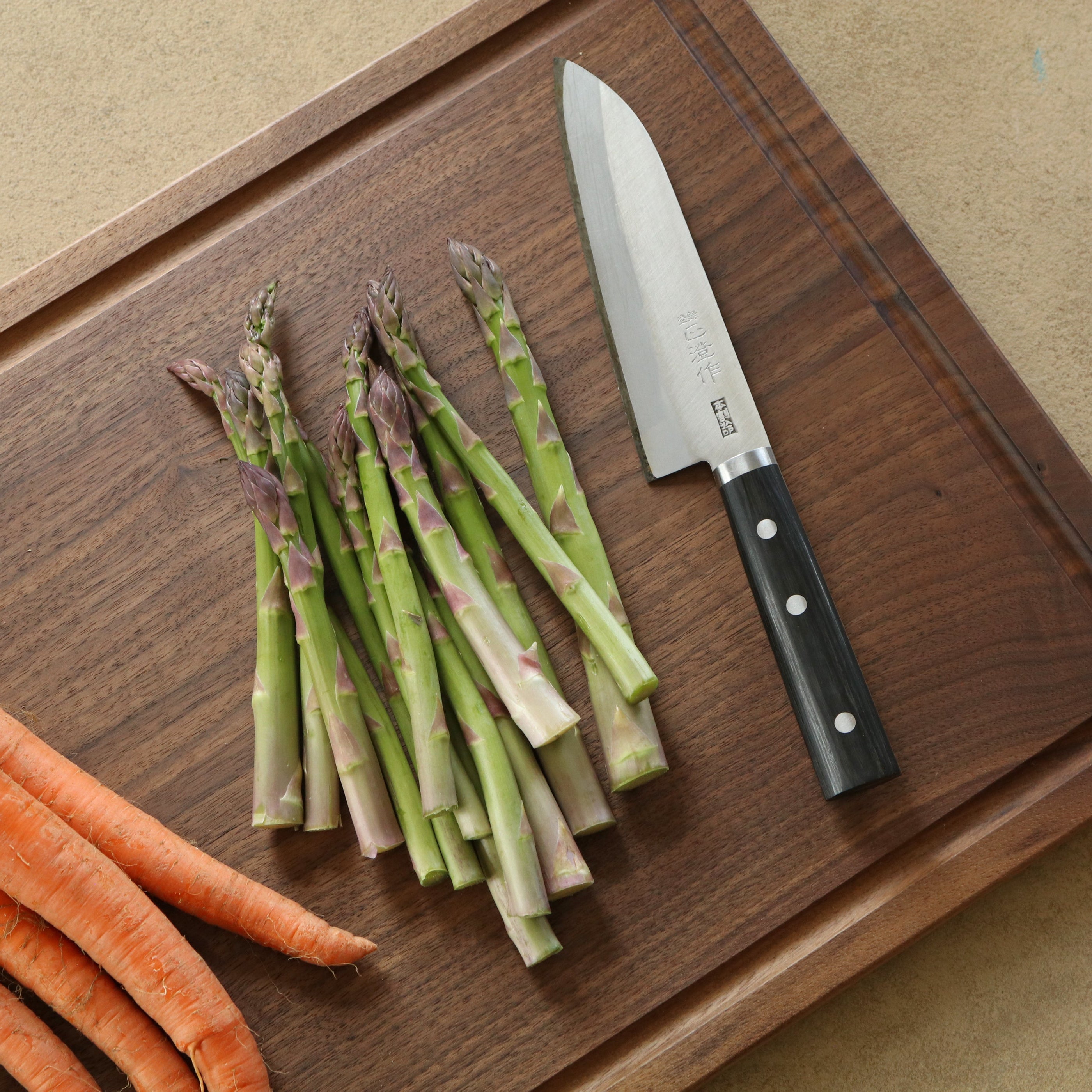 Carrots, asparagus, and a knife on a wooden cutting board.