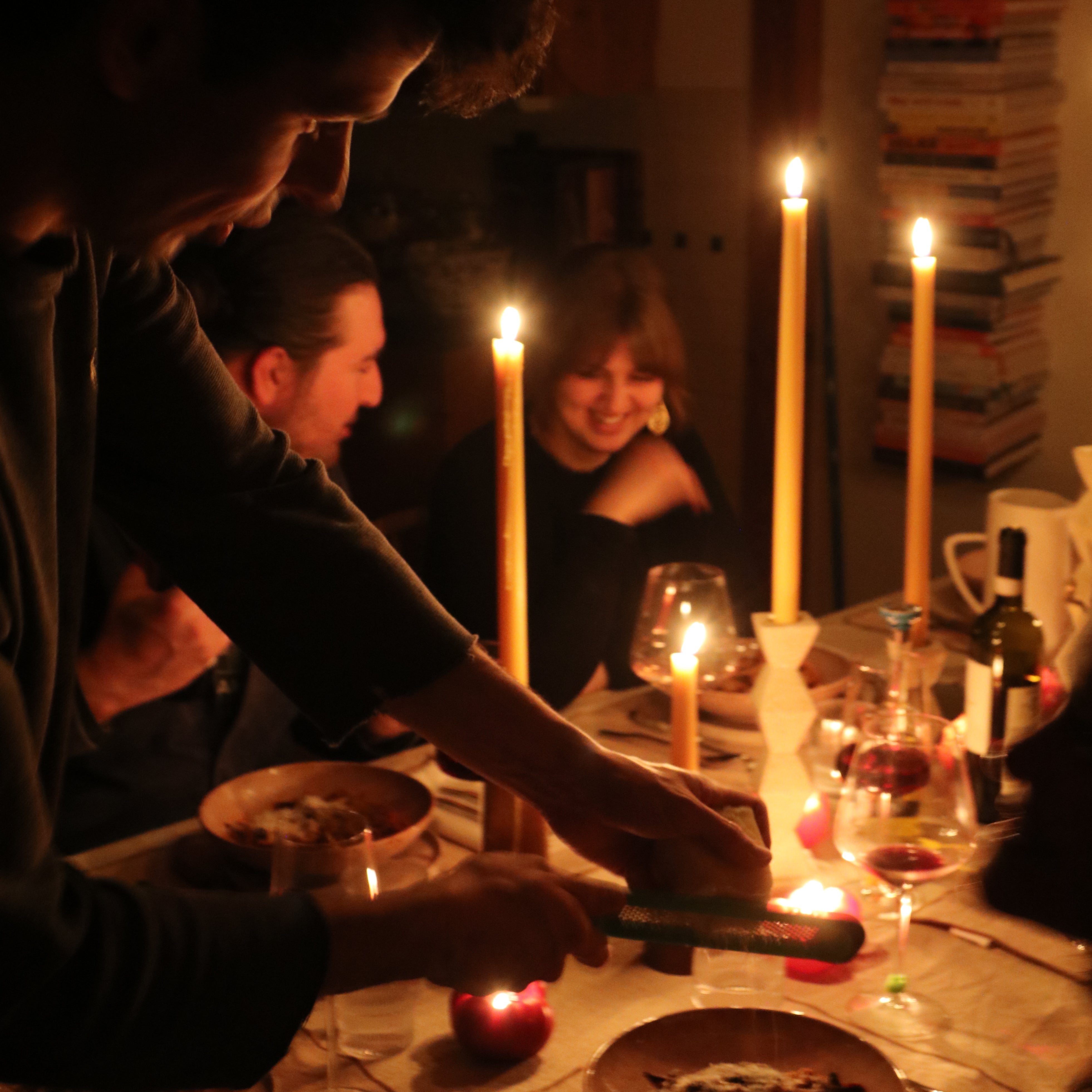 People gathered around a table with candles and food in a dimly lit room.
