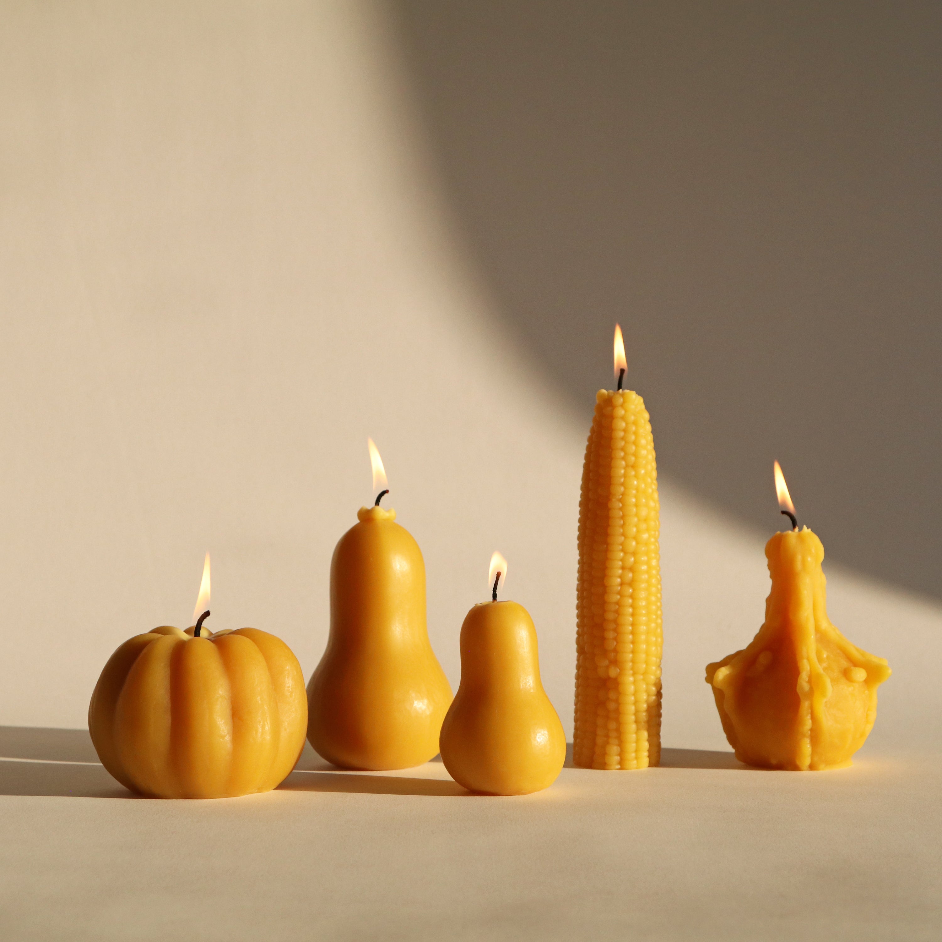 Five different shaped candles lit on a neutral background