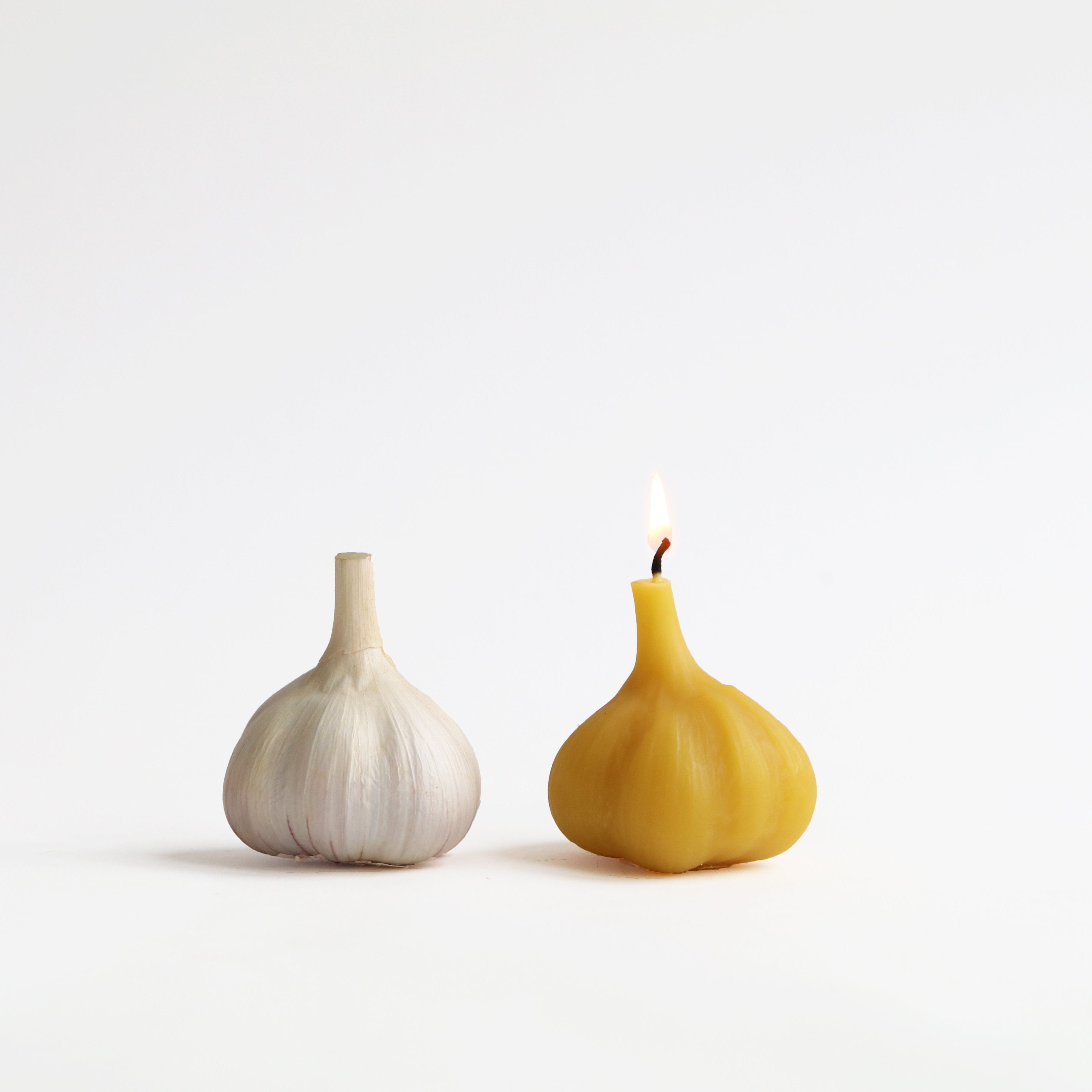 a lit garlic bulb beeswax candle next to a real garlic bulb