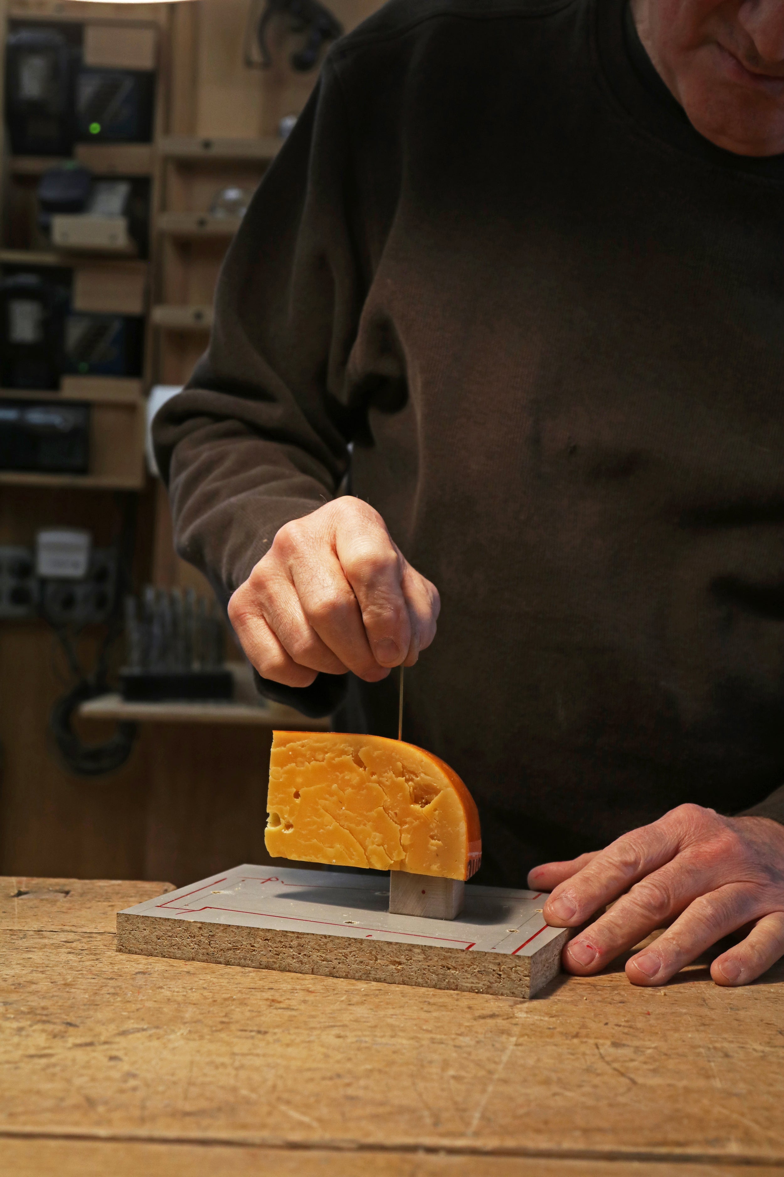 Person cutting a wedge of cheese with a knife on a wooden board.