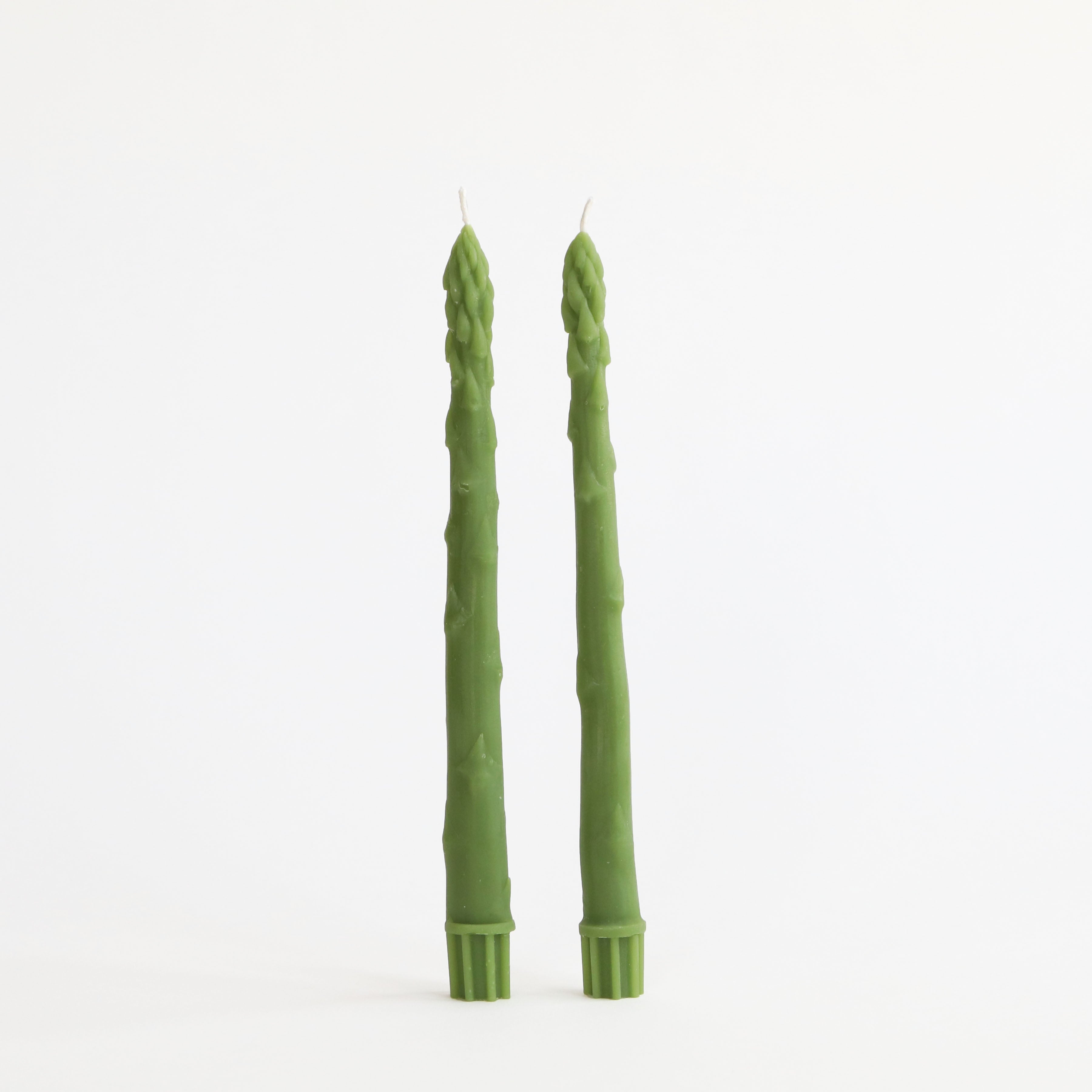 Two green candles with a textured surface on a white background