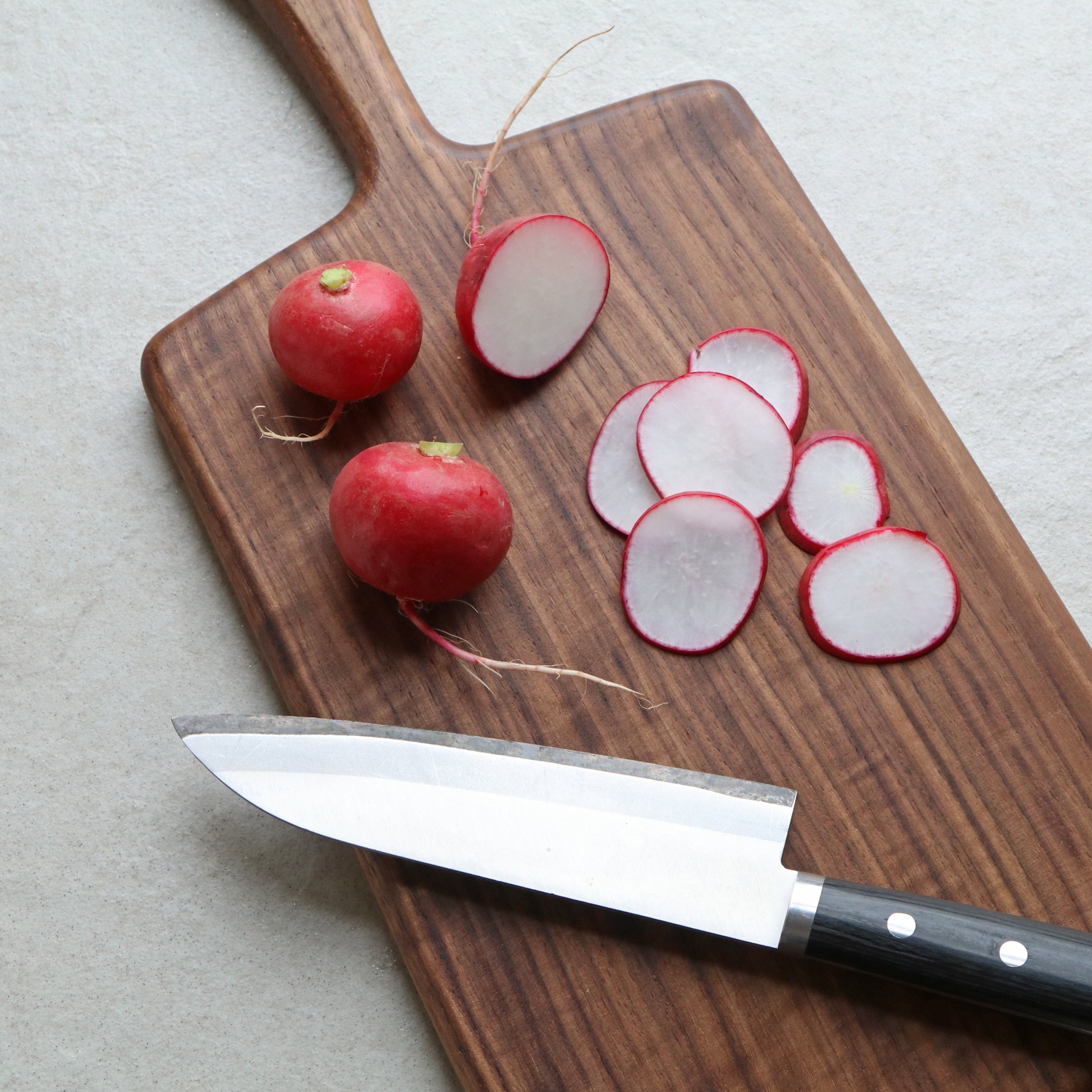 Wooden cutting board with radishes and a knife on a light gray background