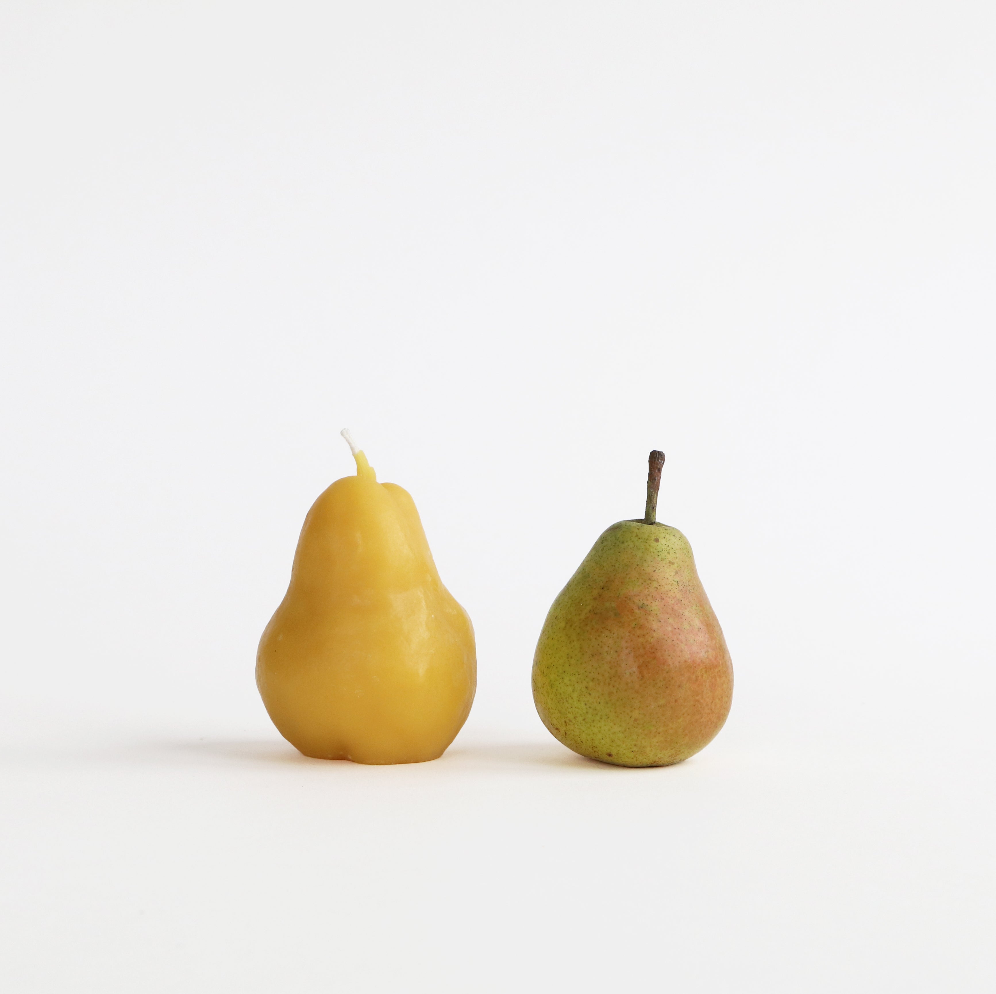 One pear candle and one green real pear on a white background