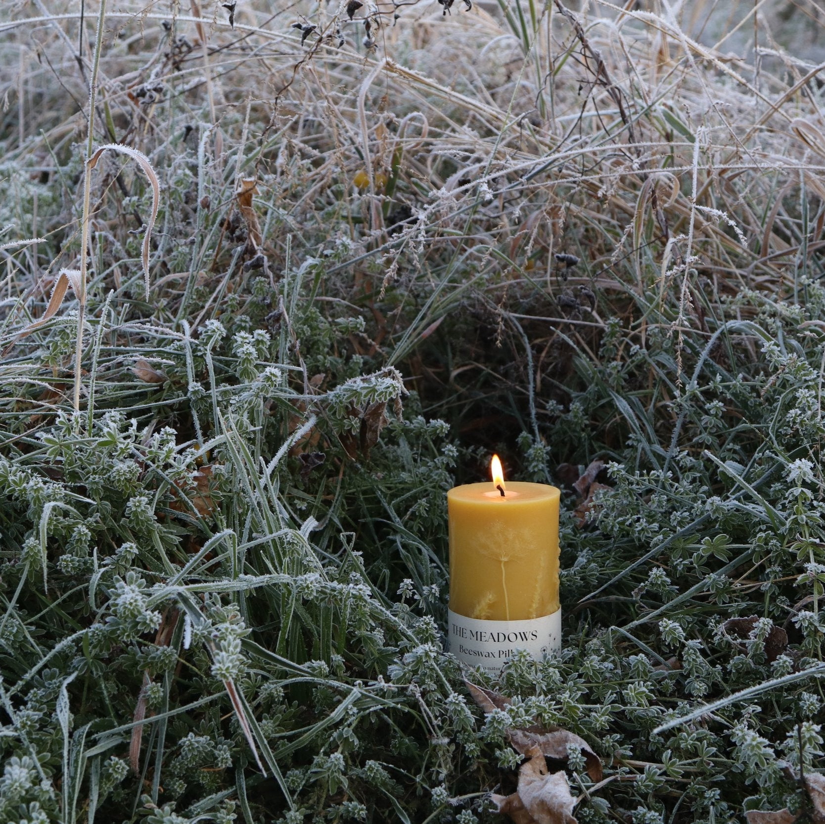 lit beeswax candle in meadow flowers