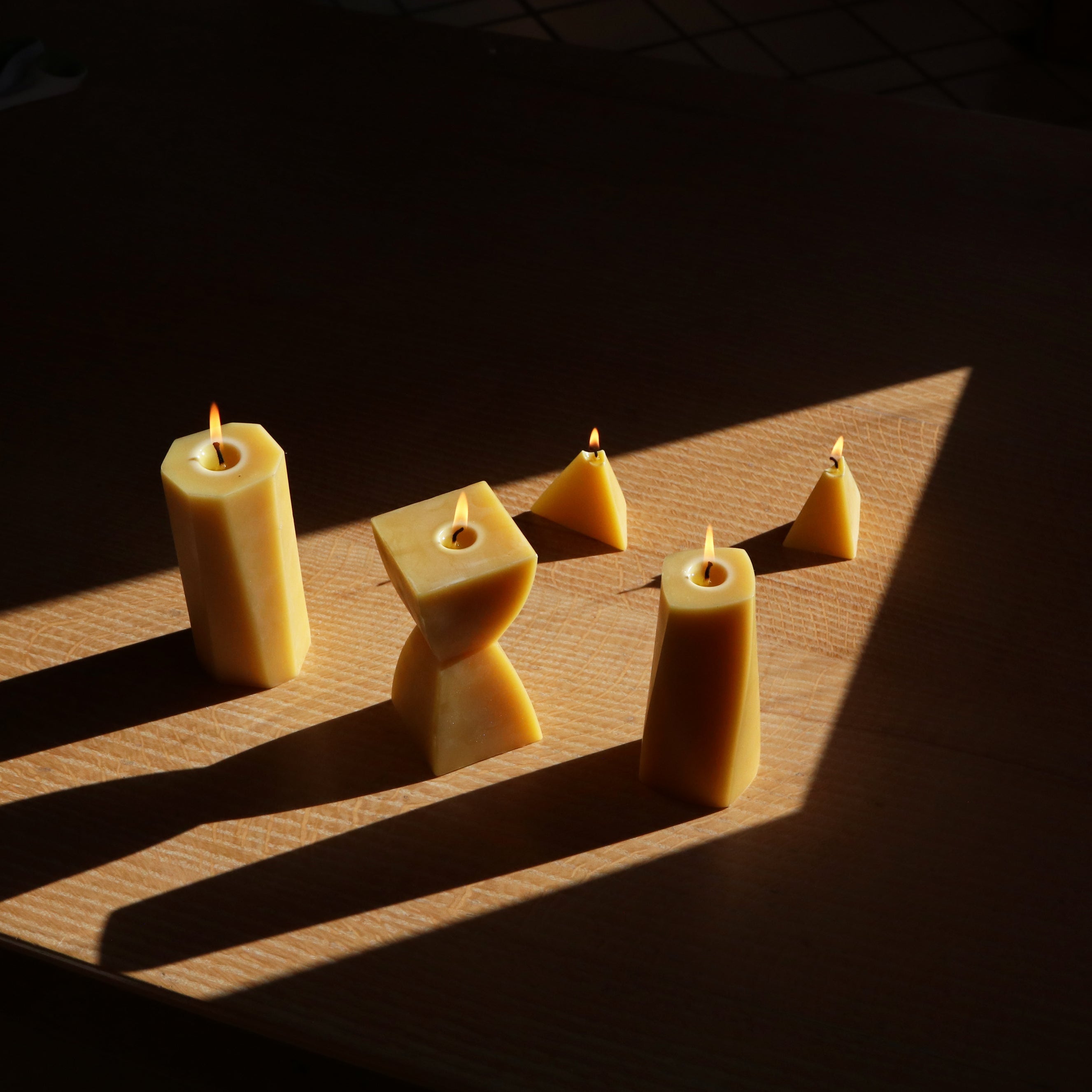 Set of beeswax candles arranged on a wooden surface with shadows cast by the light.