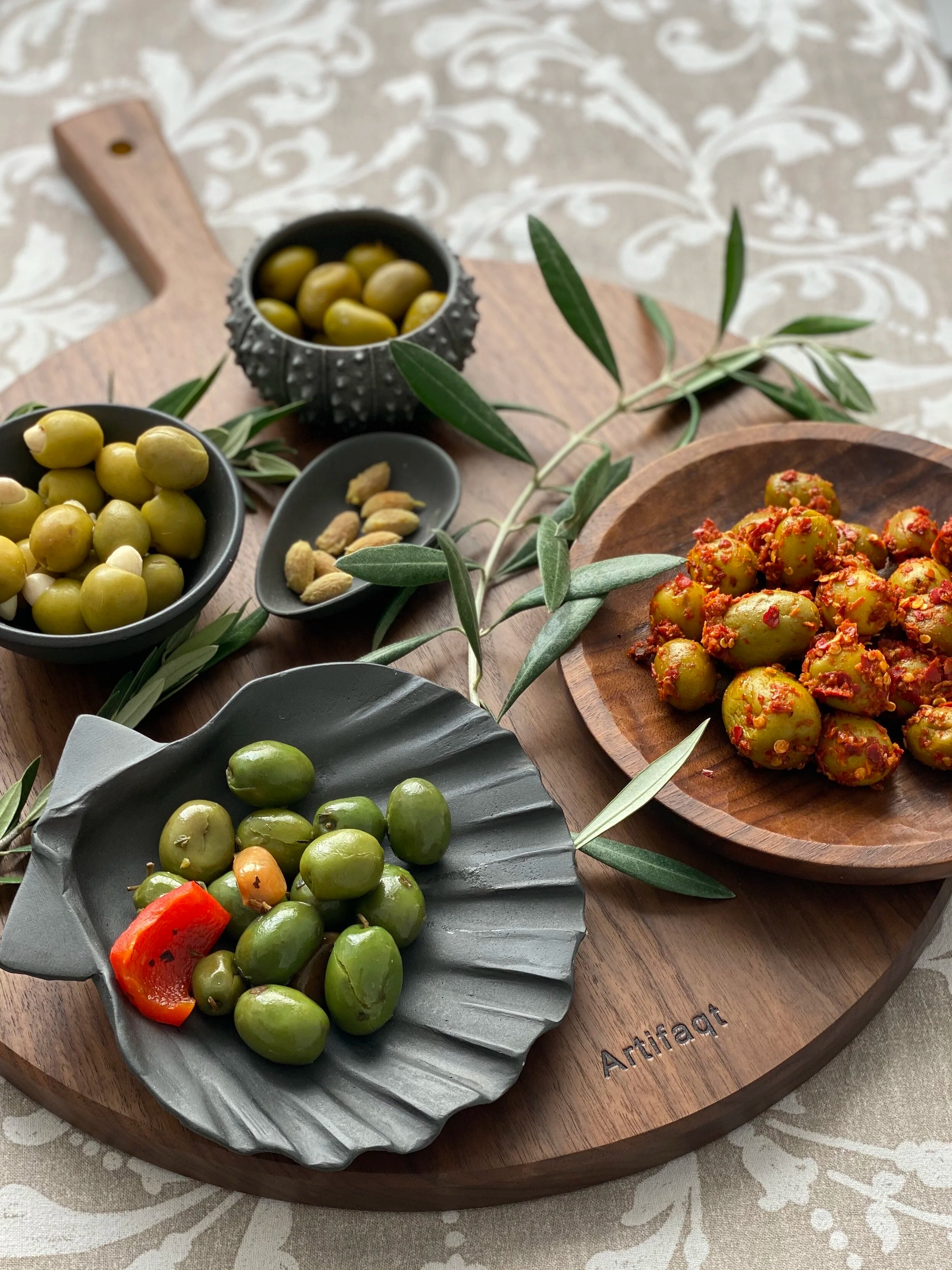 Assorted olives on decorative plates with a wooden cutting board and olive branch.