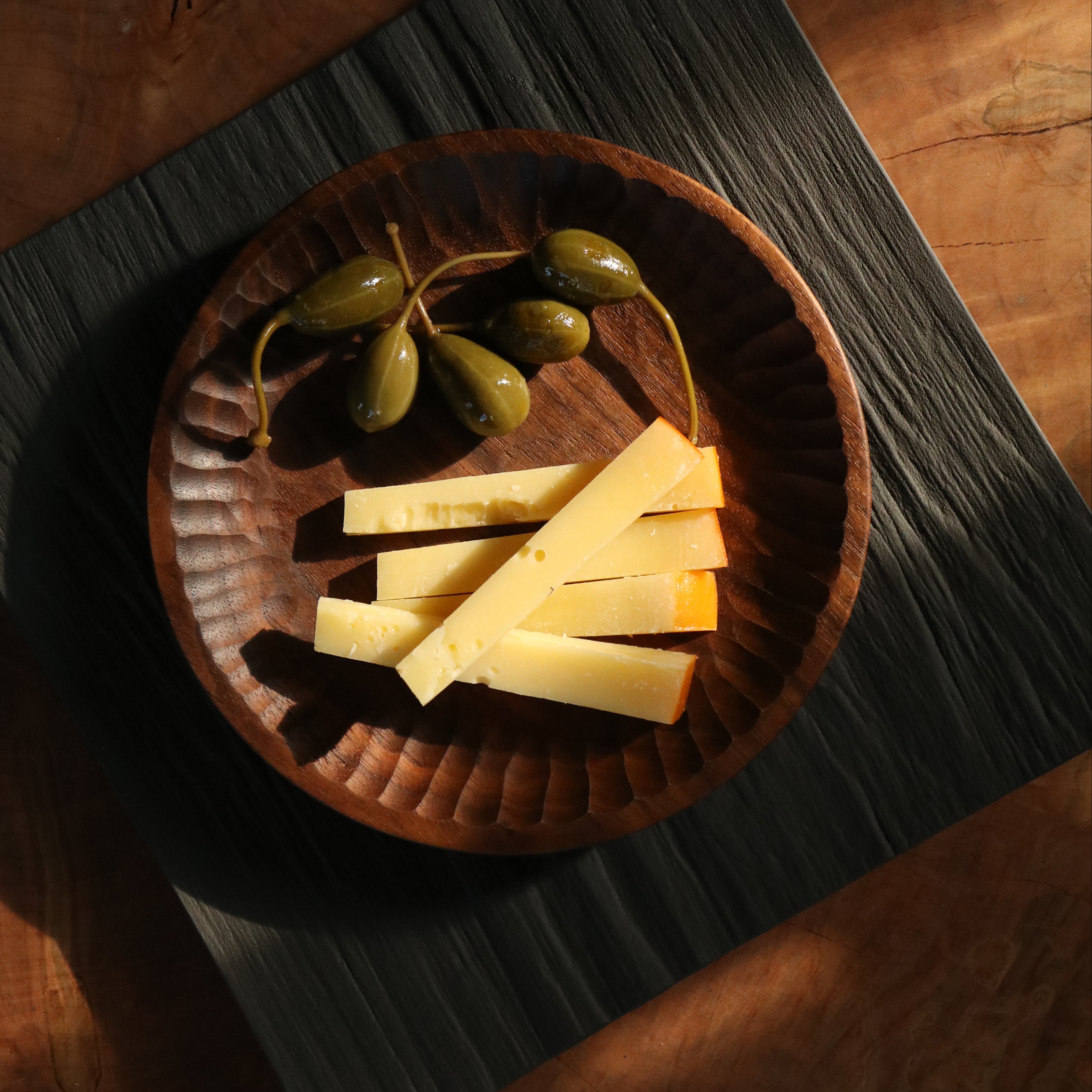Wooden plate with sliced cheese and pickles on a wooden surface