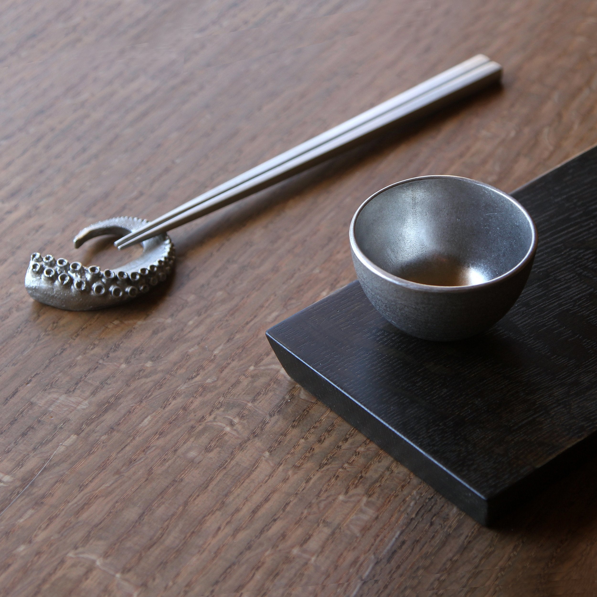 octopus chopstick rest next to small metal cup on wood platter bowl