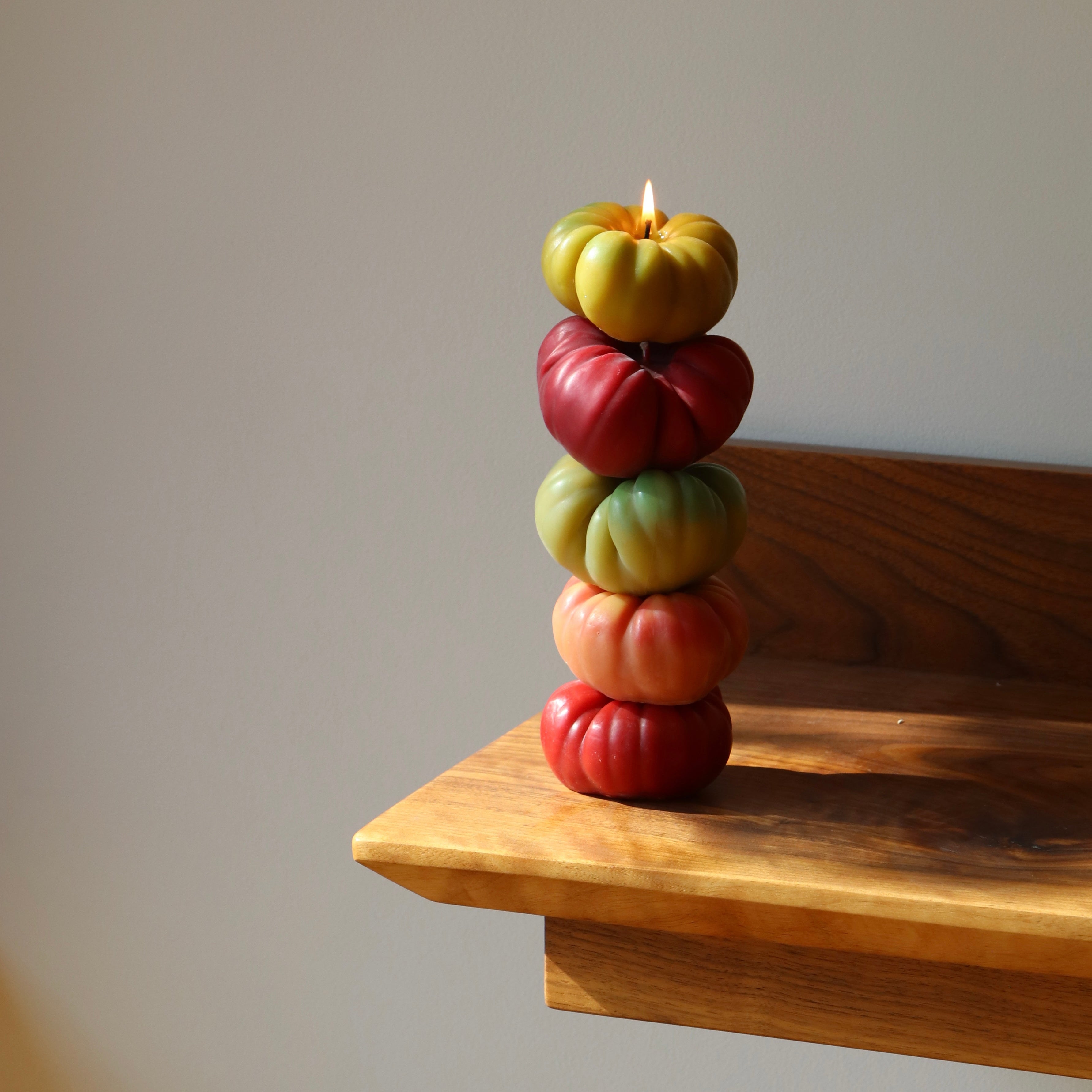 Stack of colorful fruit-shaped candles on a wooden shelf with a plain background