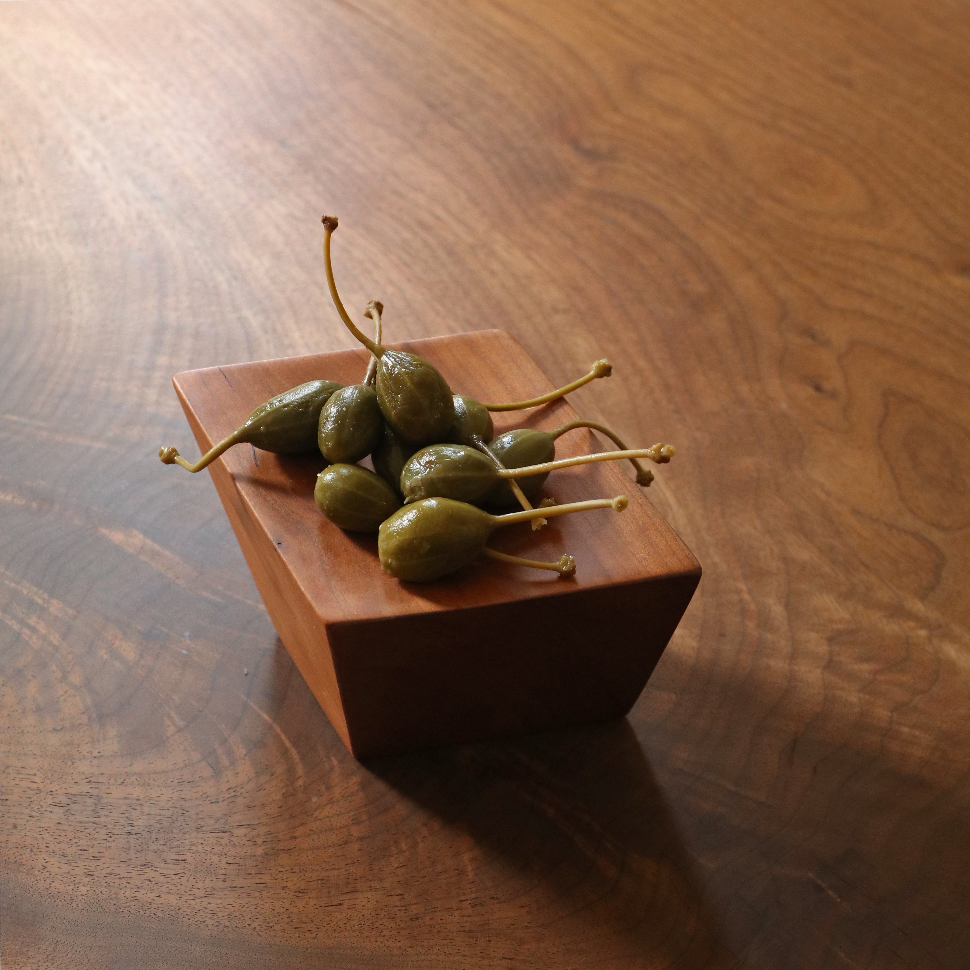 Wooden dish with green pickled items on a wooden surface