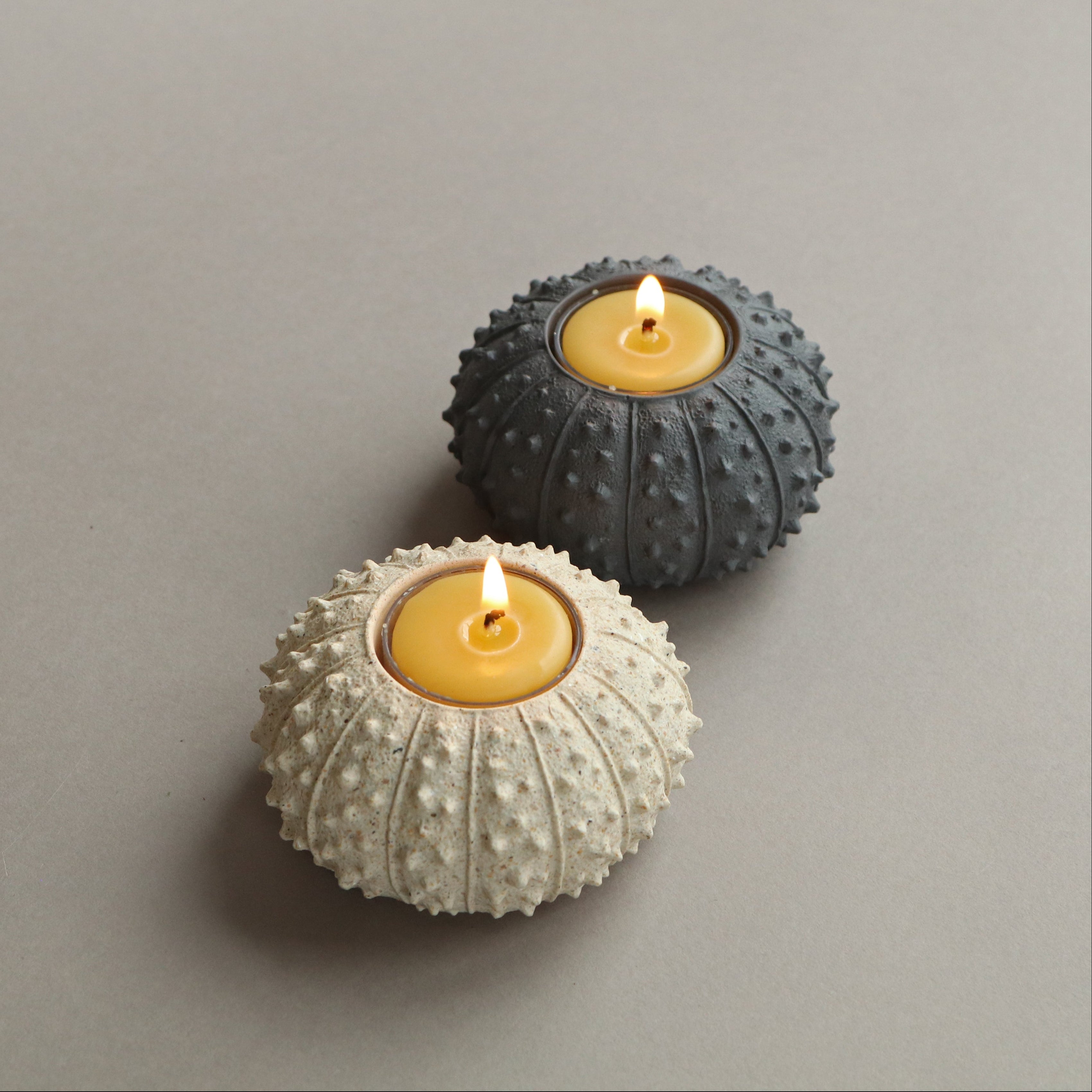 Two textured candle holders with lit candles on a gray background