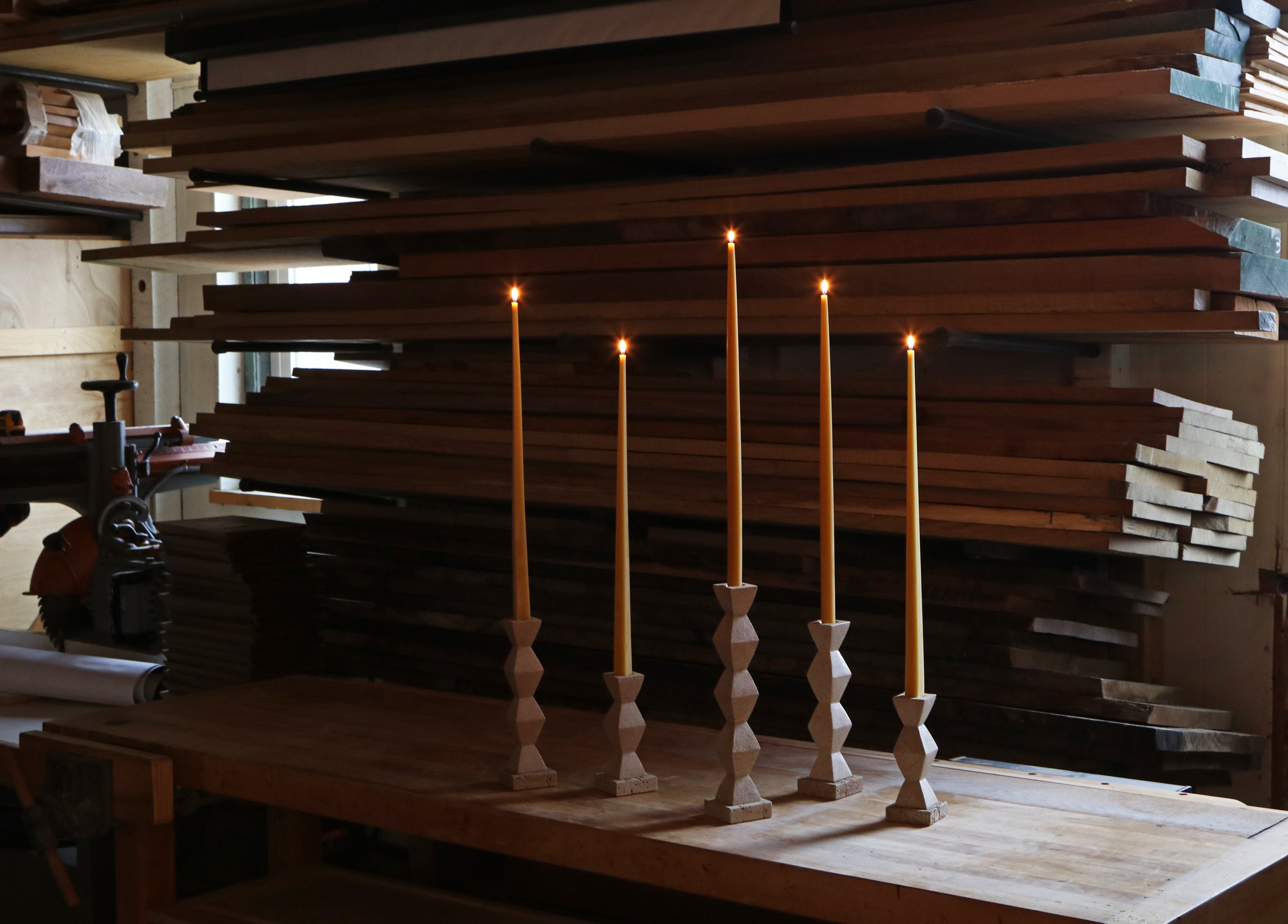 Set of wooden candlesticks on a wooden surface with stacks of wood in the background